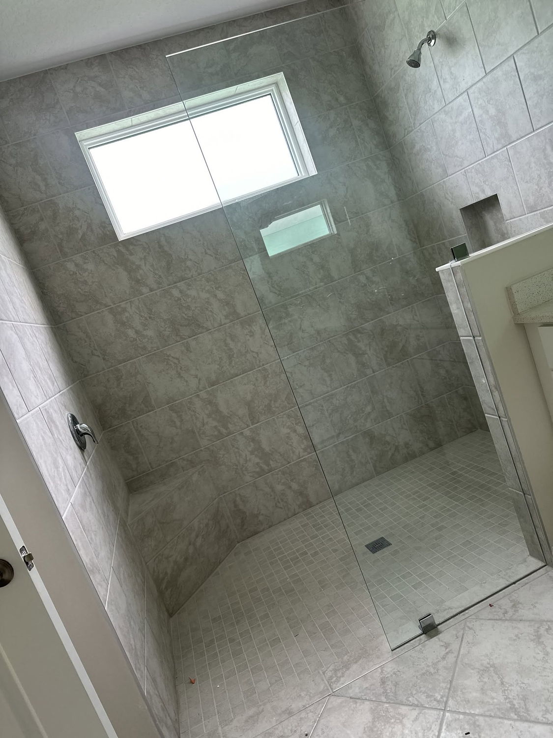 Full height gray tile walk-in shower with a glass panel and niche